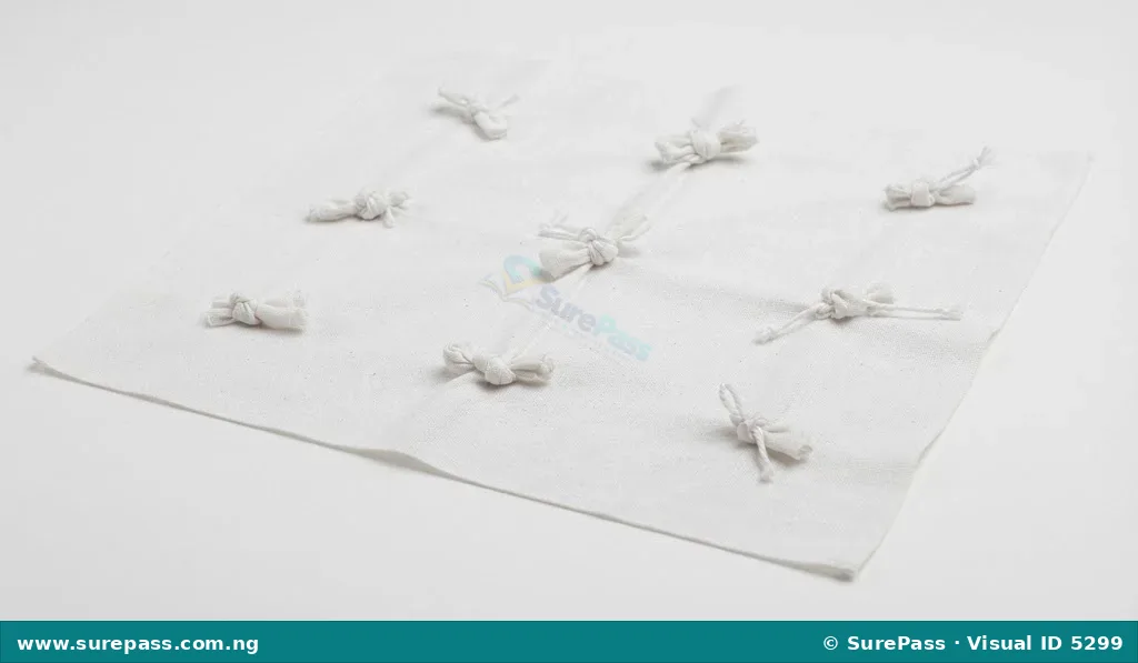White fabric with multiple small knots tied into it, demonstrating the knotting technique for tie and dye.