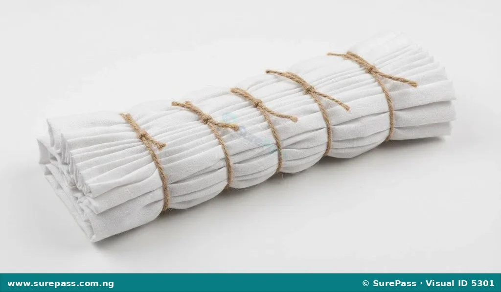 White fabric with small, parallel pleats secured by string, demonstrating a tie and dye technique.